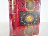 an old red book with a clock on it sitting on top of a table