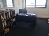 a desk with a computer and a book shelf in the corner