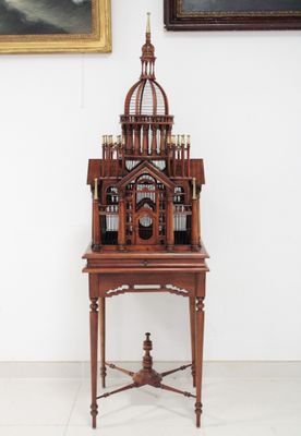 une petite cage à oiseaux en bois posée sur un socle devant un tableau