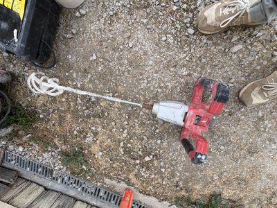 a corded drill on the ground next to a pair of shoes