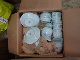 une boîte contenant des tasses à thé et des soucoupes, posée par terre