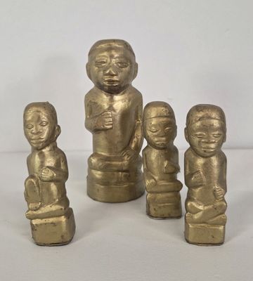 three gold figurines of children sitting on a white surface