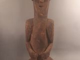 une vieille statue en bois représentant un homme assis sur une surface blanche