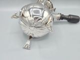 a silver teapot on a white table with a black handle