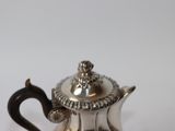 a silver tea pot with a handle on a white table