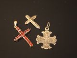 two silver and red crosses and a cross pendant on a black surface
