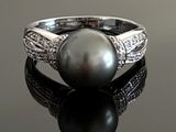 a black pearl and diamond ring on a black surface