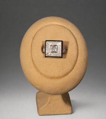 une image représentant une bague en diamant posée sur un socle, sur fond gris