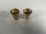 two silver shot glasses sitting on top of a white table