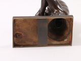 bronze sculpture of a nude woman resting on a box on a white surface