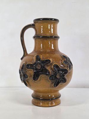 un vase brun et noir posé sur une surface blanche