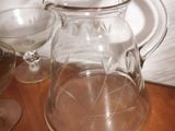 a glass pitcher sitting on a wooden table next to glasses