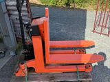 an orange forklift sitting on a pallet in front of a building