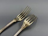 une paire de fourchettes plaquées argent posées sur une table avec un fond gris