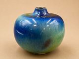 un vase bleu et vert posé sur une surface beige clair