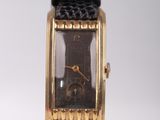 une montre en or avec un bracelet en cuir noir posée sur un fond blanc