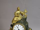 a gold clock with a woman sitting on top of it
