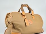 the large tan duffel bag is sitting on a white surface