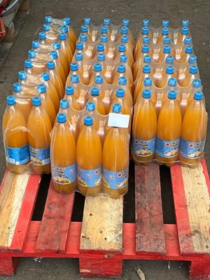 several bottles of orange juice sit on a pallet in front of a pile of wooden pallets