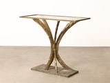 a gold console table with a glass top on a cement floor