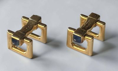 pair of gold tone cufflinks with blue stones on a white surface