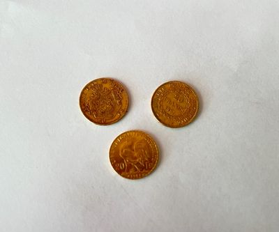 trois pièces d'or posées les unes à côté des autres sur une surface blanche