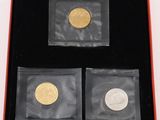 three gold and silver coins in a red box on a white surface