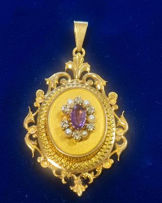 a close up of a gold pendant with a purple stone in the center