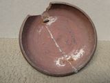 une assiette marron trouée, posée par terre
