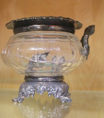 un saladier en verre avec un couvercle en argent posé sur une table en verre
