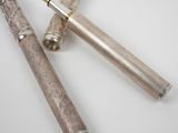 two silver colored pens sitting next to each other on a white surface