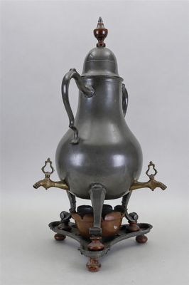une cafetière ancienne en argent posée sur un support, sur fond blanc