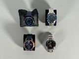 quatre montres différentes posées sur une surface blanche, à côté d'un sac noir
