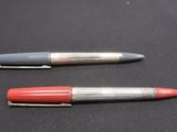 two pens sitting on top of a black surface next to each other