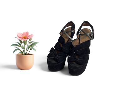 une petite fleur dans un pot, à côté d'une paire de chaussures noires
