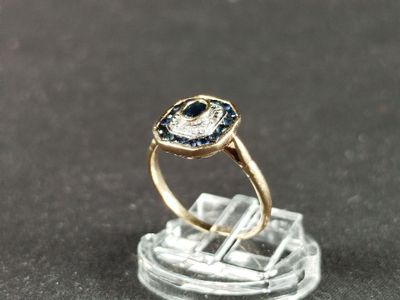 une photo d'une bague sertie d'un diamant et d'un saphir posée sur un morceau de verre transparent