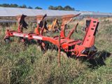 une charrue rouge attachée à un tracteur, au milieu d'un champ