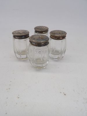 four small glass jars with silver lids sit on a white surface