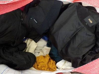un sac de vêtements posé sur un lit, à côté d'une paire de chaussures