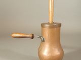 une petite casserole en cuivre munie d'une poignée en bois, posée sur une table