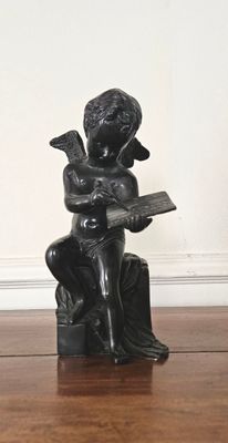 une statue représentant un garçon assis sur un rocher, en train de lire un livre