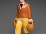 figurine of a man with a hat, jacket, and yellow pants holding a bag