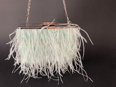 a white purse with feathers hanging from a chain on a black background
