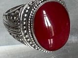 bague en argent sertie d'une pierre rouge sur un fond blanc