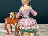 porcelain figurine of a woman sitting at a table with a basket of flowers
