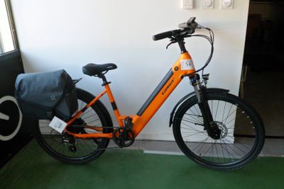 un vélo orange garé à côté d'une porte, avec un sac posé dessus