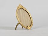 an oval mirror with a gold frame on a stand on a white surface