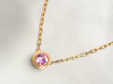 Un collier en or orné d'une pierre rose est présenté sur un fond blanc.