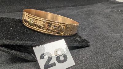 un bracelet en or portant un numéro, posé sur un tissu noir