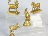 trois figurines en or représentant des animaux et un oiseau, posées sur un socle transparent